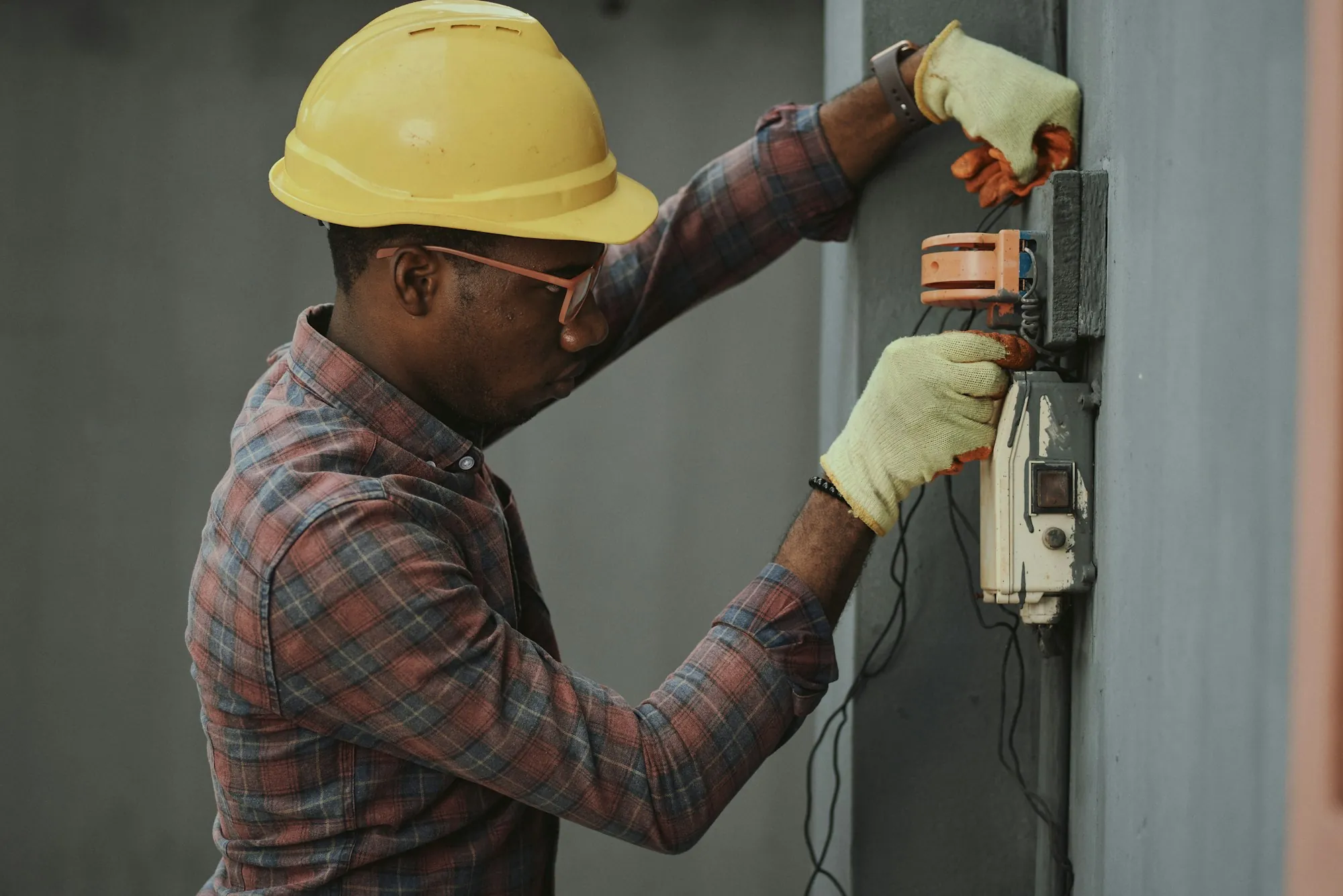 An electrician working at a wall-mounted electrical enclosure outside a house