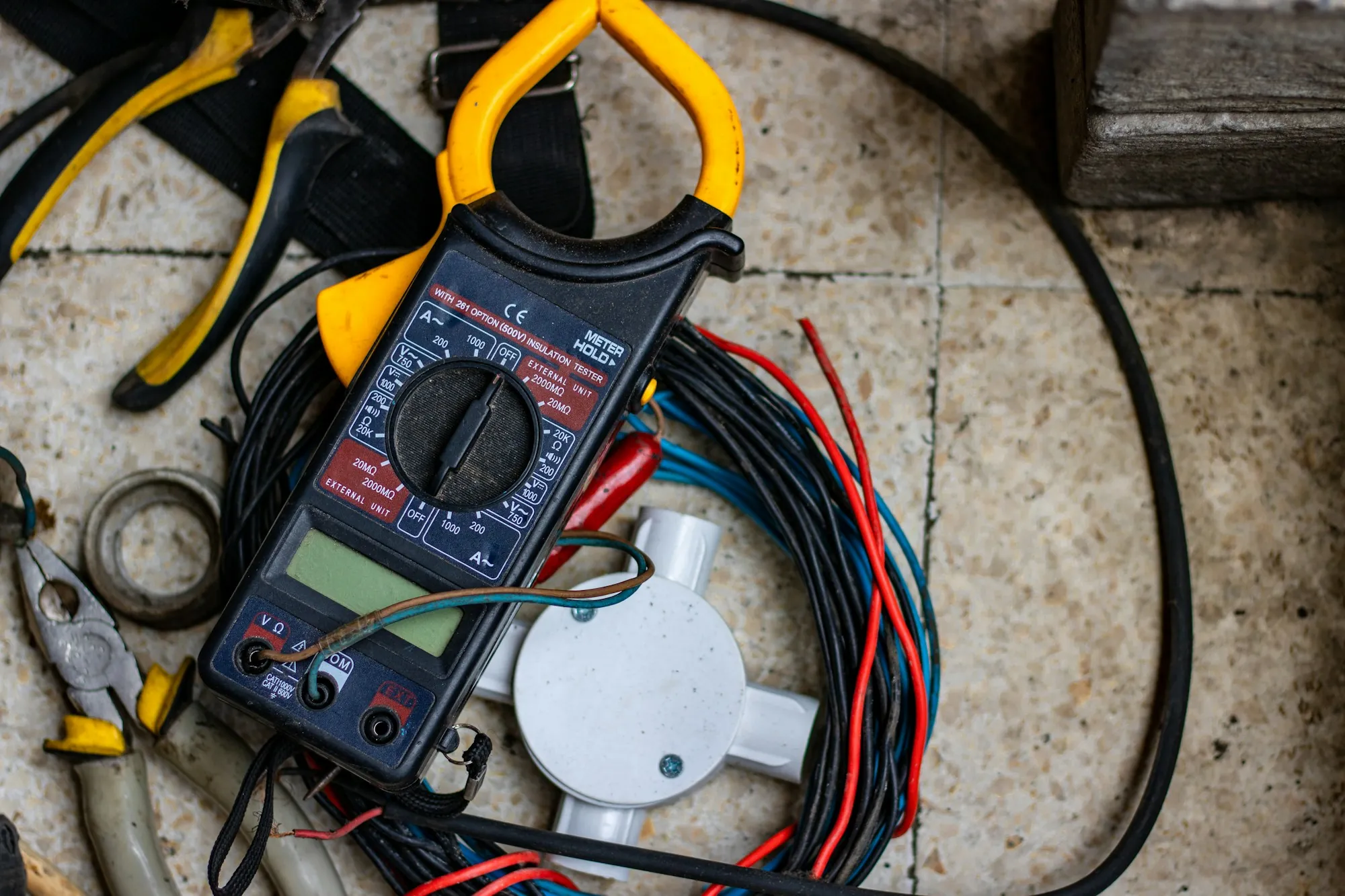 A multimeter and hand tools laid out beside coiled electrical cable